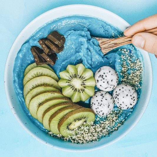 Blue smoothie bowl with kiwi slices, dragon fruit, and chocolate on a light blue background